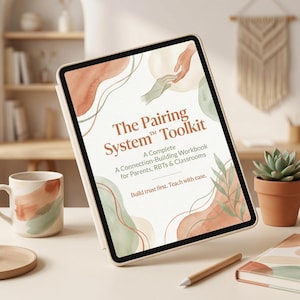 May include: A digital tablet displaying "The Pairing System Toolkit" workbook cover. The cover features watercolor-style designs in shades of peach, green, and brown. A matching mug and a small succulent in a terracotta pot are also visible.