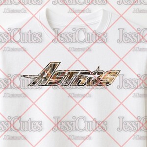 May include: White t-shirt featuring the word "Astros" in a stylized design with a camouflage pattern. The shirt has short sleeves and a crew neck.