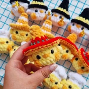 May include: Handmade crochet chick toys in yellow, white, and orange. Some chicks wear yellow and red sombreros, while others wear black and yellow witch hats. The chicks have black eyes and are made of soft yarn.