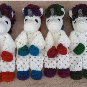 May include: Four handmade crochet unicorn dolls. Each unicorn has a white body, a colorful mane, and a horn. The dolls have different colored mittens and feet, including red, blue, green, and purple. The dolls are arranged in a row.
