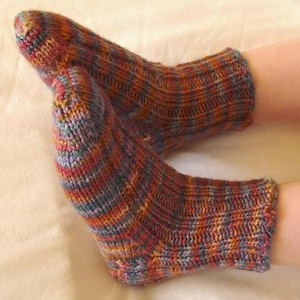 May include: A pair of hand-knitted socks with a striped pattern in shades of red, orange, blue, and yellow. The socks have a textured appearance, with ribbed cuffs and heels. The yarn creates a warm, cosy feel.