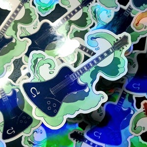 May include: A collection of stickers featuring a black electric guitar design with a wave and the Greek letter omega. The stickers have a holographic finish and are surrounded by green and white wave-like shapes.