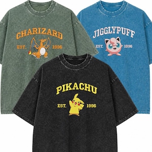 Può includere: Tre magliette oversize in verde, blu e nero. Ogni maglietta presenta un personaggio Pokémon diverso: Charizard, Jigglypuff e Pikachu, con il nome del personaggio e l'anno 1996 stampati sul davanti.