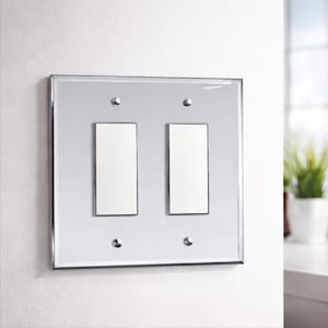 May include: A mirrored light switch plate with two rectangular light switch openings. The plate has a silver frame and four silver screws. The light switches are white. The plate is mounted on a white wall.