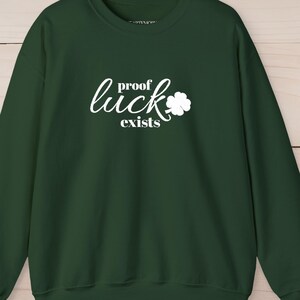 May include: A dark green sweatshirt with the words "proof luck exists" in white script and a white shamrock graphic. A white shamrock is also on the left sleeve.