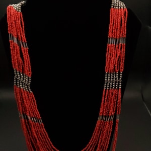 May include: A multi-strand necklace composed of small, vibrant red beads. The necklace features sections of silver-colored beads and is displayed on a black mannequin. The beads cascade down, creating a layered effect.