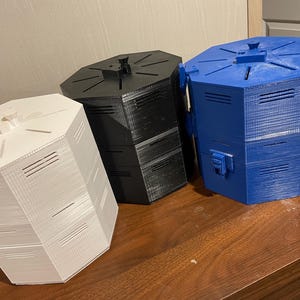 May include: Three hexagonal containers in white, black, and blue. Each has a lid with a central handle and slotted vents. The containers are made of a textured material and sit on a wooden surface.