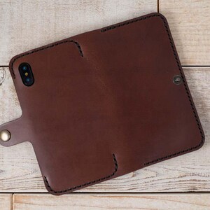 May include: A brown leather phone case with a stitched edge and a flap closure. The case has a small metal button on the flap.