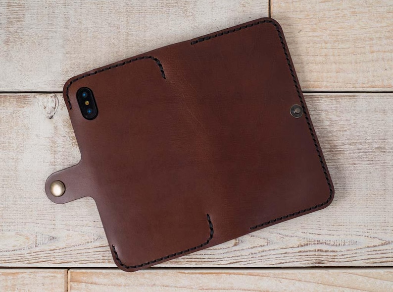 May include: A brown leather phone case with a stitched edge and a flap closure. The case has a small metal button on the flap.