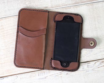 May include: A brown leather phone case with a built-in wallet. The case has two card slots and a flap that closes with a snap. The phone case is designed to fit a smartphone with a screen size of approximately 5.5 inches.