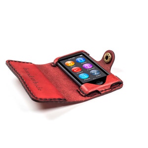 May include: Red leather case with a snap closure for an iPod. The case has the words "Handschilde" embossed on the front.