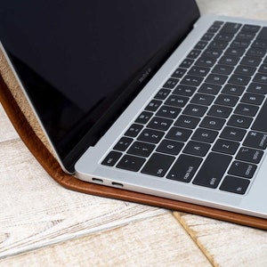 May include: A silver laptop with a black keyboard rests inside a brown leather case. The laptop screen is black and open, displaying a portion of the keyboard. The case has a textured appearance.