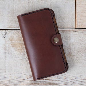 May include: A brown leather wallet with a snap closure and a stitched edge.
