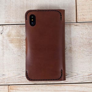 May include: A brown leather phone case with stitching around the edges. The case has a cutout for the camera lens.