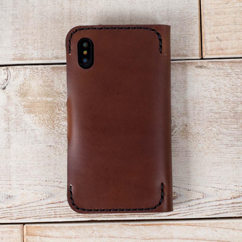 May include: A brown leather phone case with stitching around the edges. The case has a cutout for the camera lens.