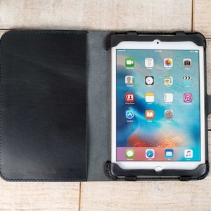 May include: Black leather case for a tablet with a screen showing a variety of apps. The case has a flap that folds over the screen and a button on the side.