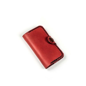 May include: A red leather key holder with a button closure. The key holder has black stitching around the edges.