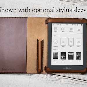 Könnte beinhalten: Eine braune Ledertasche für einen E-Reader mit einem Stiftfach. Die Tasche ist geöffnet und der E-Reader ist sichtbar. Der E-Reader-Bildschirm zeigt den Startbildschirm mit Symbolen für Notizen, Bücher, Kalender und Einstellungen. Der Text "mobcribe" ist auf dem E-Reader sichtbar.