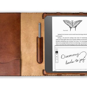 May include: A brown leather case with a pocket on the front and a pen holder on the right side. The case is open and a black e-reader with a gray stylus is inside. The e-reader screen shows a butterfly drawing and the text "Discovery leads to joy".