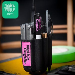 May include: Black nylon walkie-talkie caddie with a pink label that reads "Walkie-Caddie." The caddie holds a multi-tool, a pen, and other accessories. A green and white logo is in the upper left corner.