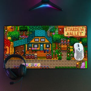 May include: A rectangular Stardew Valley mousepad featuring a pixelated scene of a house, characters, and the game's logo. A white mouse and black headset are on the pad. The pad has a black textured surface.
