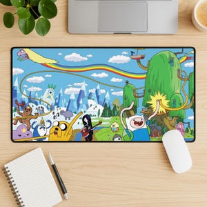 May include: A rectangular mousepad featuring a colorful cartoon scene with characters, mountains, and a rainbow against a blue sky. The mousepad has a black border and is on a wooden desk.