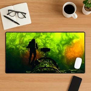 May include: A rectangular mouse pad featuring a silhouette of a person in a spacesuit against a swirling green and yellow background. The design includes a detailed structure and a white computer mouse.