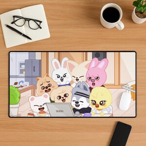 以下が含まれることがあります： ラップトップの周りに集まった、さまざまな動物のキャラクターの漫画イラストが描かれた長方形のマウスパッド。 マウスパッドは黒い縁取りで、キッチンのシーンがある明るい色の背景です。