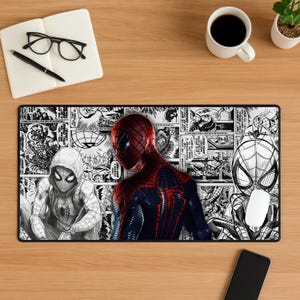 May include: A rectangular desk mat featuring a black and white comic book panel background with three Spider-Man figures. One figure is in full colour with a red and blue suit, while the other two are black and white line art illustrations.