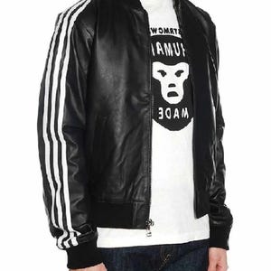 May include: Black leather bomber jacket with white stripes on the sleeves. The jacket has a ribbed collar, cuffs, and hem. A white t-shirt with a graphic print is visible underneath the jacket.