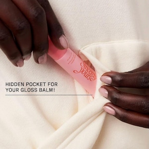 May include: A pink lip gloss tube with the text "Sincerely Yours" is placed in a hidden pocket of a cream-colored garment. The image highlights the pocket's design for storing the gloss balm.