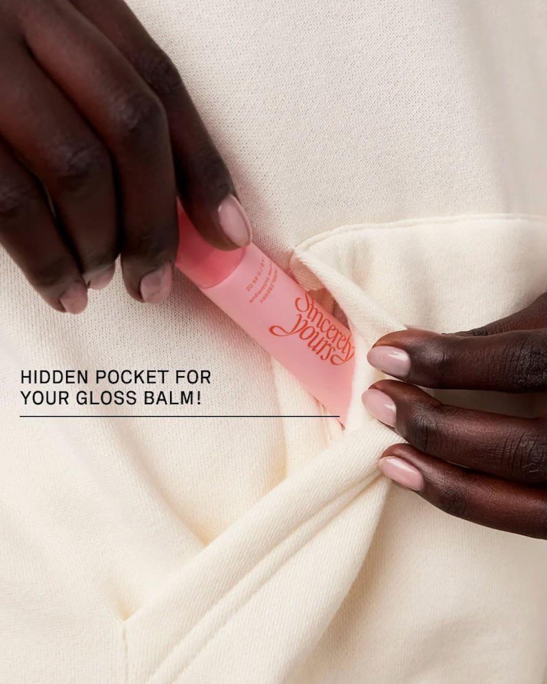 May include: A pink lip gloss tube with the text "Sincerely Yours" is placed in a hidden pocket of a cream-colored garment. The image highlights the pocket's design for storing the gloss balm.