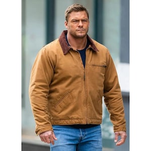 May include: A tan work jacket with a brown corduroy collar, a zipped front, and a chest pocket. The jacket is worn over a dark blue shirt and paired with blue jeans. The jacket appears to be made of a durable, heavy-duty material.
