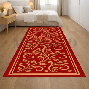 May include: A rectangular red rug with a gold floral pattern and border. The rug is placed on a hardwood floor in a bedroom setting, with a bed and nightstands visible in the background. The rug's dimensions are approximately 10 feet long.