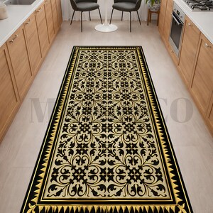 May include: A rectangular black and gold kitchen rug with an ornate floral pattern. The rug has a black border with gold accents and a repeating geometric design. The rug is placed in a kitchen with wooden cabinets and a window.