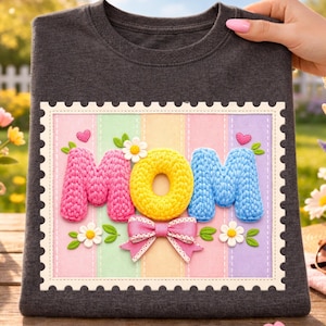 Könnte beinhalten: Dunkelgraues T-Shirt mit einem farbenfrohen Design mit der Aufschrift "MOM". Das Design zeigt die Buchstaben M, O und M in Rosa, Gelb und Blau, mit einer Schleife und Blumen. Ein schönes Geschenk zum Muttertag.