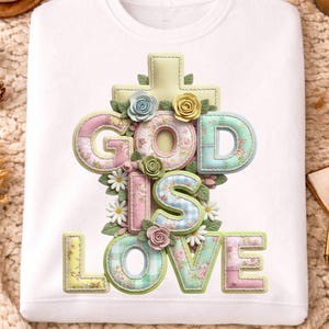 以下が含まれることがあります： 白いスウェットシャツに「GOD IS LOVE」の文字が花柄でデザインされています。文字はパステルカラーで、花と十字架で囲まれています。快適でスタイリッシュな衣服です。