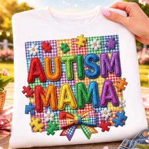 Puede incluir: Sudadera blanca con las palabras "AUTISM MAMA" en letras coloridas y texturizadas. El diseño incluye piezas de rompecabezas, flores y un fondo a cuadros. Un lazo a cuadros arcoíris está en la parte inferior.