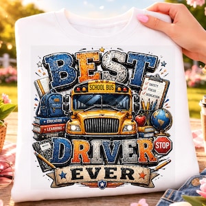Op de afbeelding: Witte sweatshirt met een kleurrijke afbeelding met de tekst "BEST DRIVER EVER". Het ontwerp toont een gele schoolbus, boeken, een wereldbol en de woorden "SAFETY, FOCUS, DEDICATION". De sweatshirt wordt door een persoon omhoog gehouden.