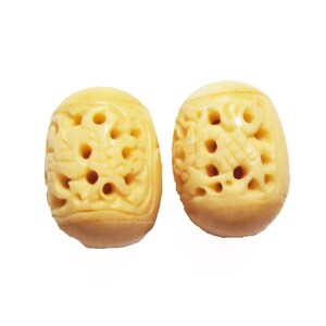 May include: Two carved, oval-shaped beads with a cream-colored finish. Each bead features intricate openwork designs and multiple holes. The beads are displayed against a white background.