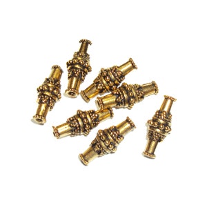 May include: A group of seven gold-toned metal beads with intricate designs. The beads are cylindrical and have a textured surface.