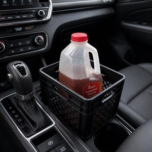 May include: A clear plastic jug of sweetened iced tea with a red cap sits in a black plastic crate inside a car. The jug has a handle and a label that reads "Sweetened Iced Tea". The crate is placed in the center console of the car.