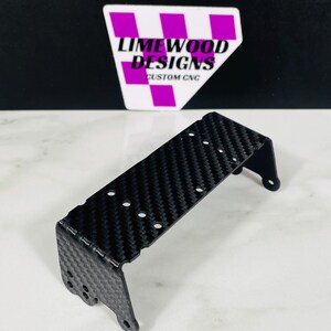 May include: A black carbon fiber bracket with multiple holes and a textured surface. The bracket has a bent design with two small circular holes on the sides. The background features a logo that says "LIMewood DESIGNS CUSTOM CNC".