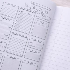May include: Open notebook with a detailed daily planner layout. The left page features sections for goals, time blocking, water intake, and a money tracker. The right page is lined for notes. The planner includes sections for weather and mood tracking.