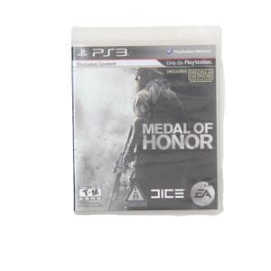 May include: A PS3 game case for "Medal of Honor." The cover shows a soldier with a weapon, in a grayscale design. Includes "Medal of Honor Frontline." The game is in a clear plastic sleeve.