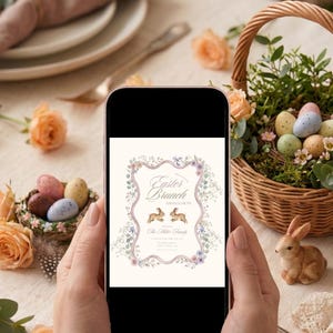 Puede incluir: Una persona sostiene un teléfono inteligente que muestra una invitación para un brunch de Pascua. La invitación presenta detalles florales, dos ilustraciones de conejos y el texto "Easter Brunch and Egg Hunt". La escena incluye una cesta de huevos, rosas y un conejo de cerámica.