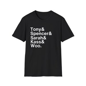 May include: Black crew neck t-shirt with white text. The text includes the names Tony, Spencer, Sarah, Kass, and Woo, arranged vertically. The shirt is made of a soft material and is suitable for casual wear.