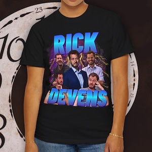 May include: A black short-sleeve t-shirt featuring a graphic print of Rick Devens in various poses. The text RICK DEVENS appears in large, bright blue gradient lettering over a background of purple clouds and yellow lightning bolts.