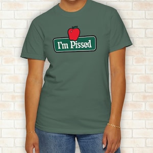 May include: A dark green t-shirt featuring a red apple above a green sign with the text "I'm Pissed" in white. The shirt is a crew neck style and is being worn by a person.