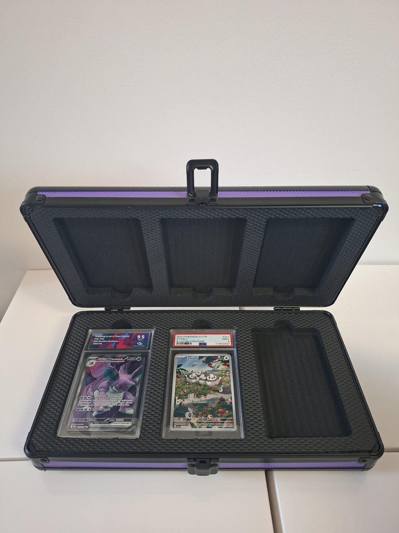 Puede incluir: Malet&iacute;n negro abierto para tarjetas con ribete morado, que contiene dos cartas coleccionables calificadas. El malet&iacute;n tiene un asa e inserciones de espuma para asegurar las tarjetas.